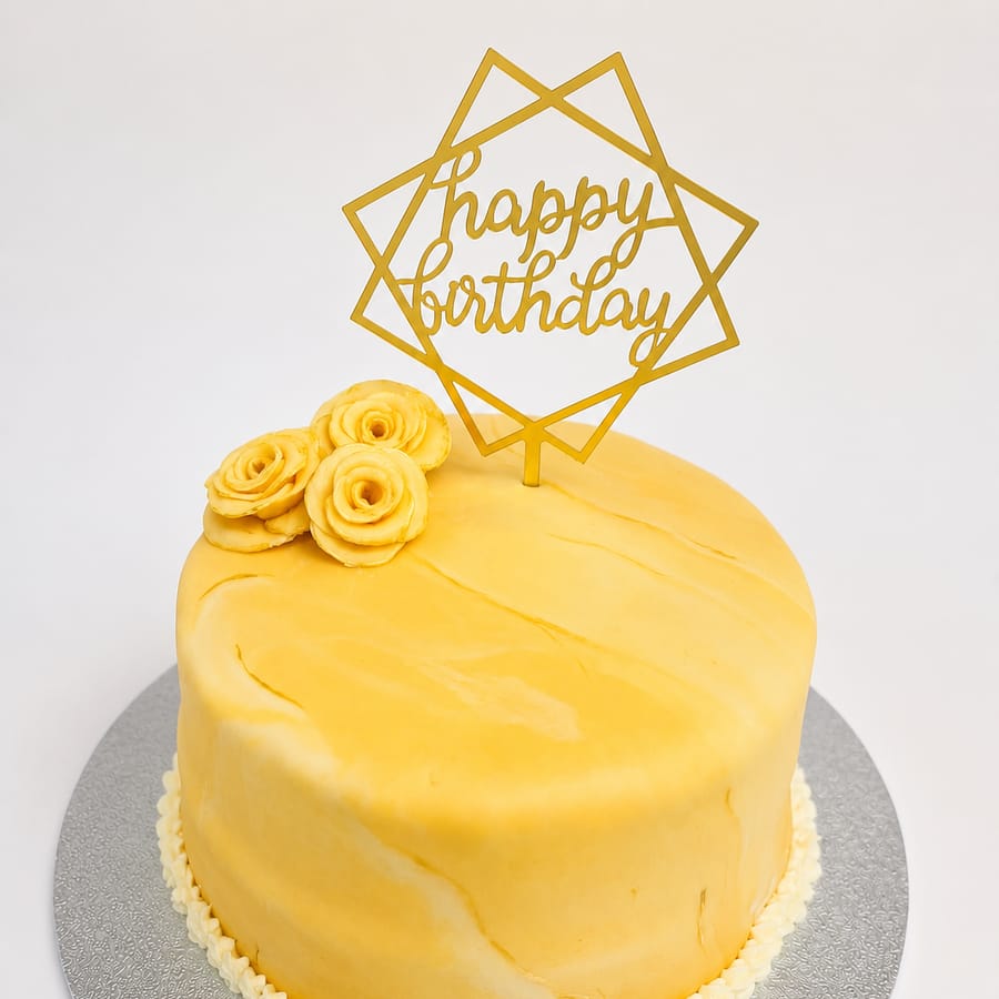 A sunshine-yellow fondant birthday cake topped with hand-piped roses and a gold topper