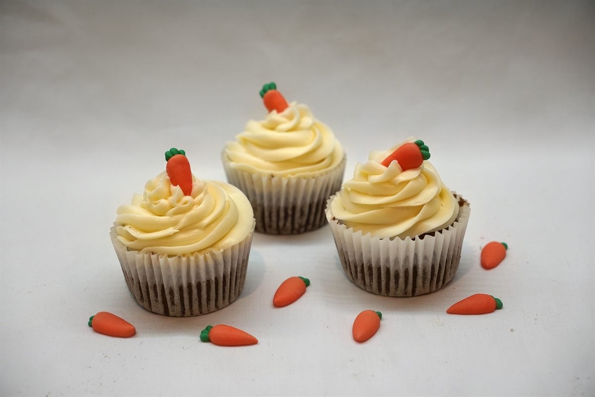 Three carrot cake cupcakes swirled with cream-cheese frosting, each topped with a tiny sugar carrot
