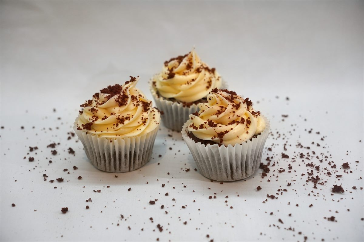 Three red velvet cupcakes swirled with cream-cheese frosting and dusted with red velvet crumb