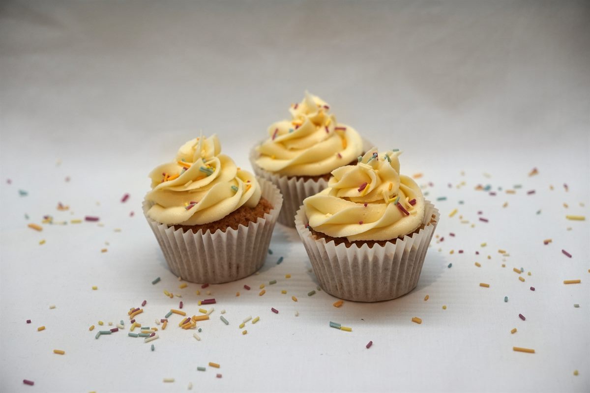 Three vanilla cupcakes piped with tall buttercream swirls and scattered with colourful sprinkles